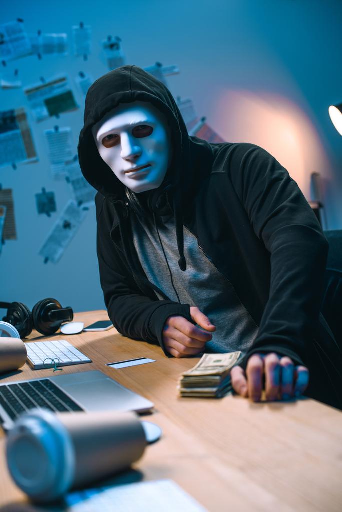 Masa üzerinde para yığını ile maskeli hacker - Fotoğraf, Görsel