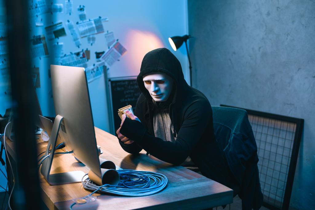 з капюшоном хакер в масці підрахунок вкрадених грошей на своєму робочому місці
 - Фото, зображення