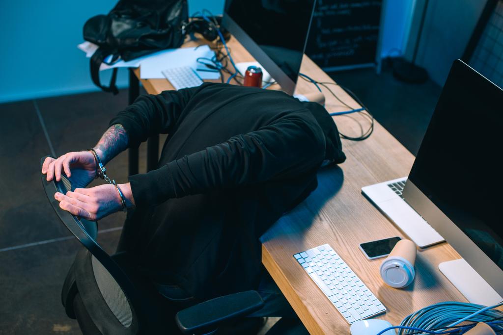 hacker esposado con capucha apoyado en su escritorio
 - Foto, imagen