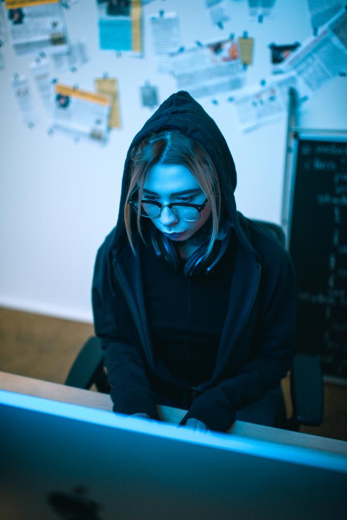 Blick aus der Vogelperspektive auf junge Hackerin, die unter Blaulicht Malware entwickelt - Foto, Bild