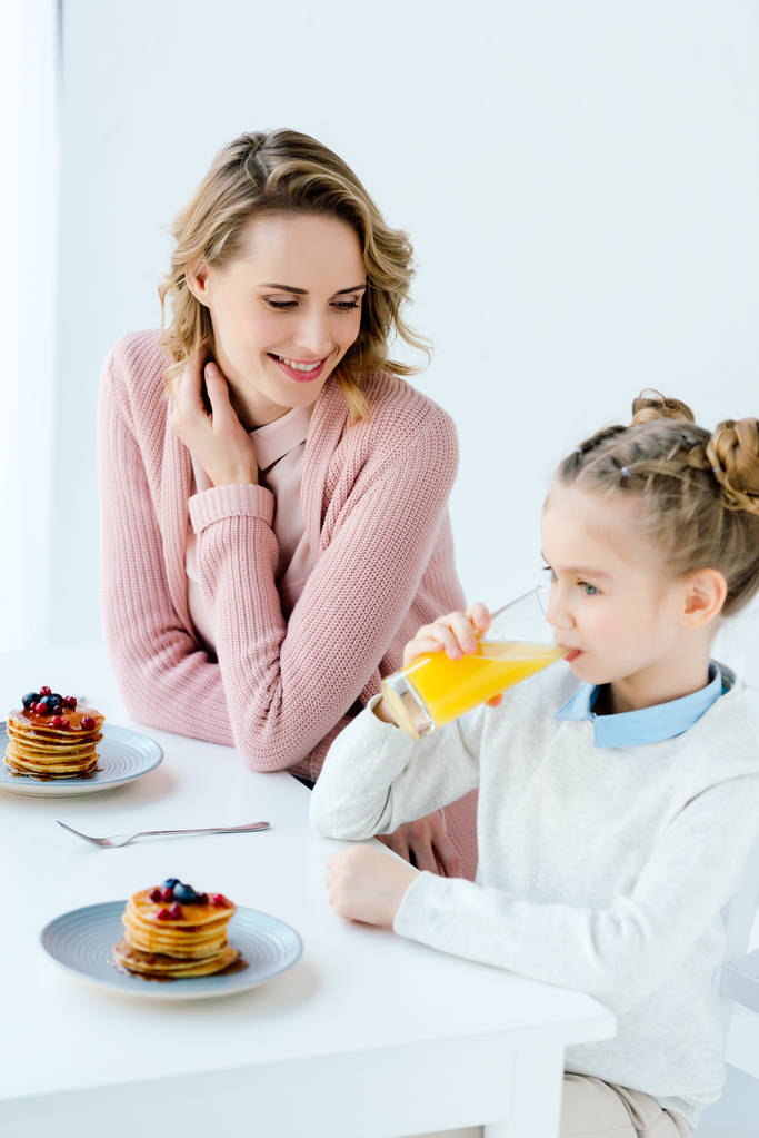Улыбающиеся мать и дочь завтракают вместе за столом
 - Фото, изображение