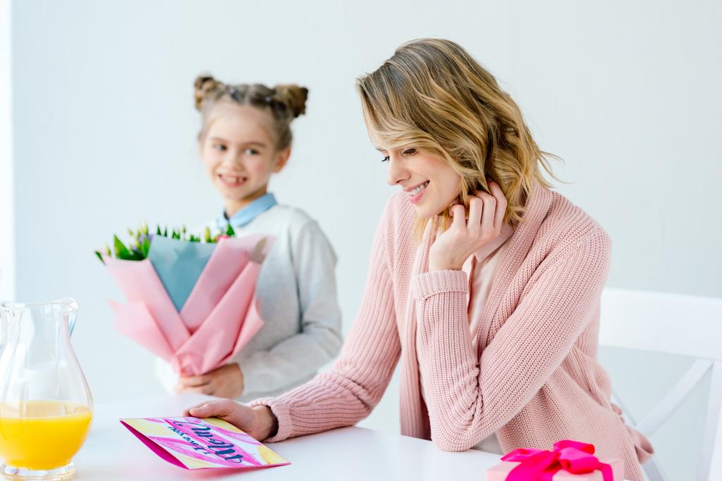 вибірковий фокус щасливої матері, дивлячись на листівку і дочку з букетом квітів, що стоїть поруч, концепція Дня матері
 - Фото, зображення