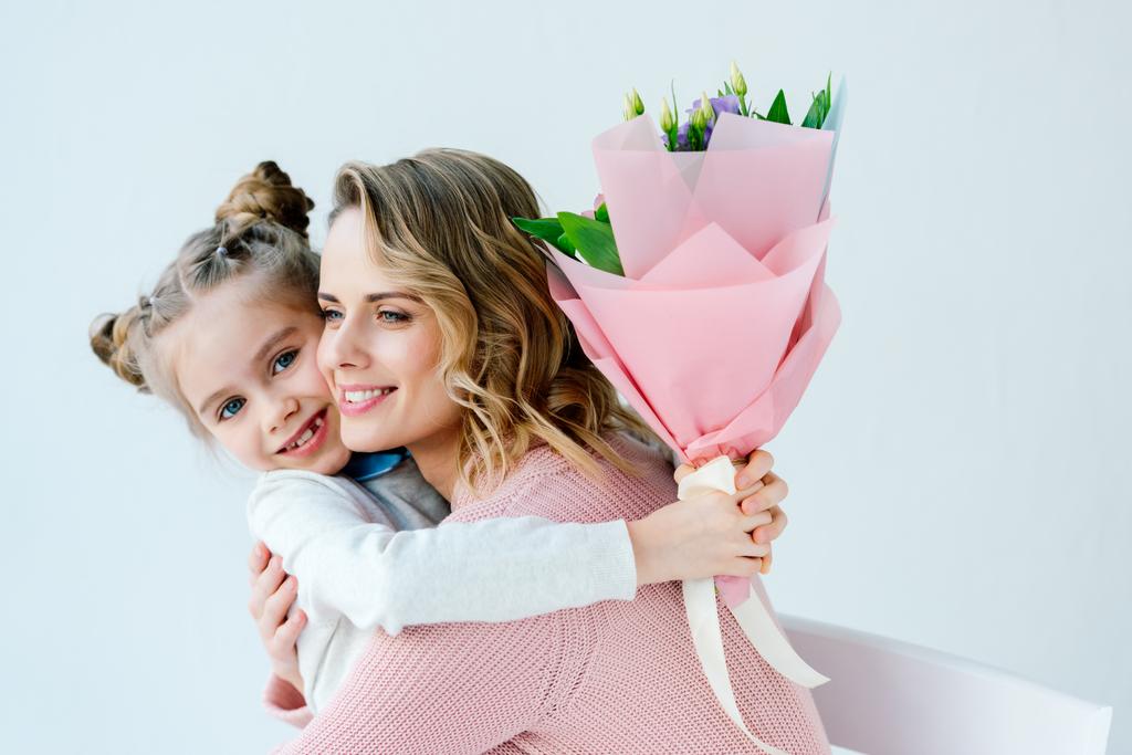 portrait of smiling daughter with bouquet of flowers and happy mother hugging each other, happy mothers day concept - Photo, Image