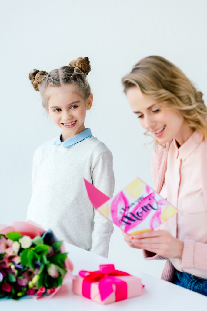 улыбающаяся женщина читает поздравительную открытку с маленькой милой дочкой, стоящей рядом, концепция Дня матери праздник
  - Фото, изображение