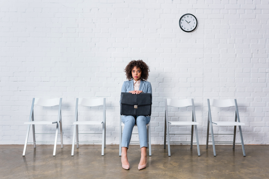 angespannte Geschäftsfrau mit Aktentasche auf Stuhl sitzend und wartend - Foto, Bild