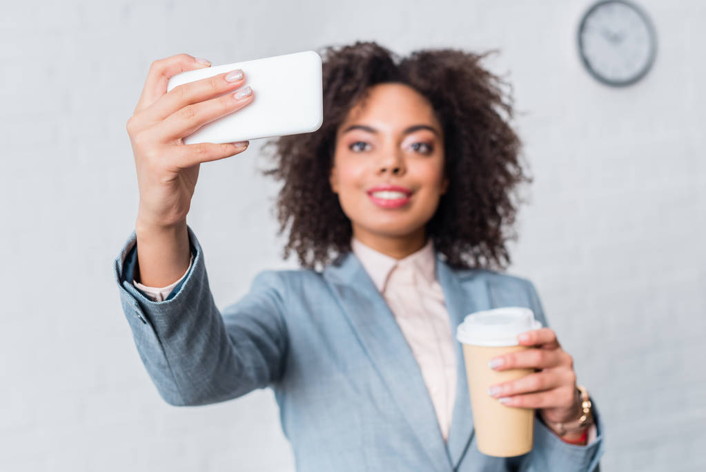 Businesswoman in suit holding coffee cup and taking selfie - Photo, Image