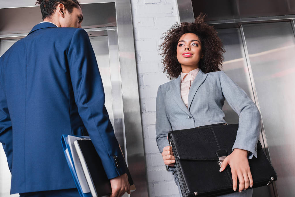 African american businesswoman with briefcase and man with folders waiting by elevator - Photo, Image