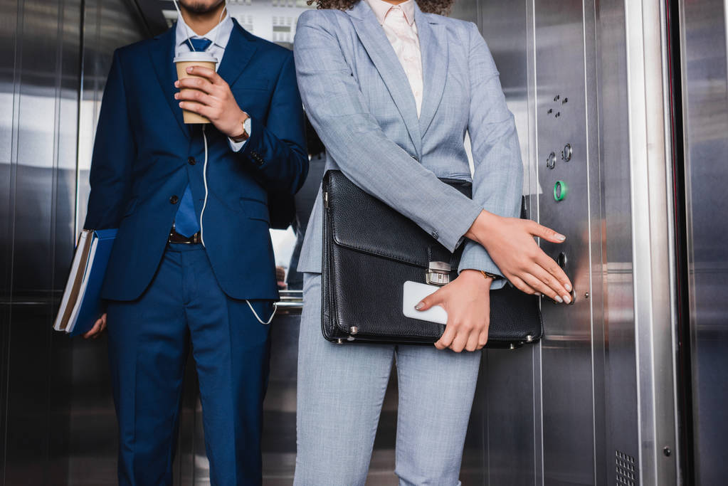 Крупный план деловой женщины, нажимающей кнопку в лифте мужчиной в наушниках с кофейной чашкой
 - Фото, изображение