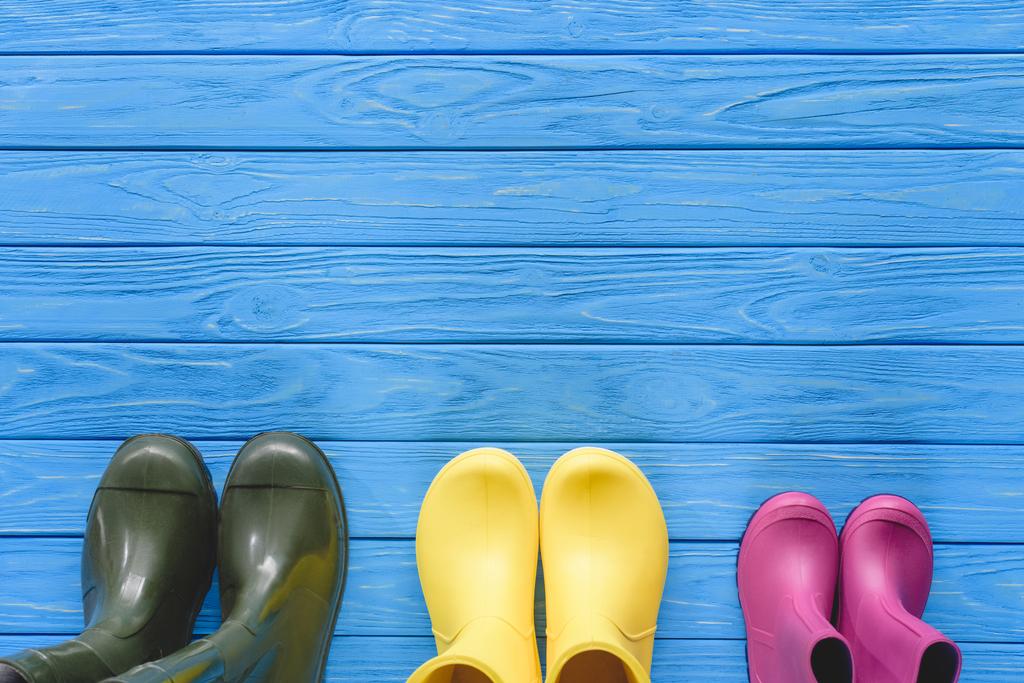 bovenaanzicht van kleurrijke rubberen laarzen in rij op blauwe houten planken geplaatst - Foto, afbeelding