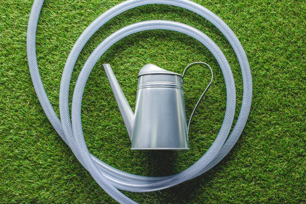 top view of watering can surrounded by hose on grass  - Photo, Image