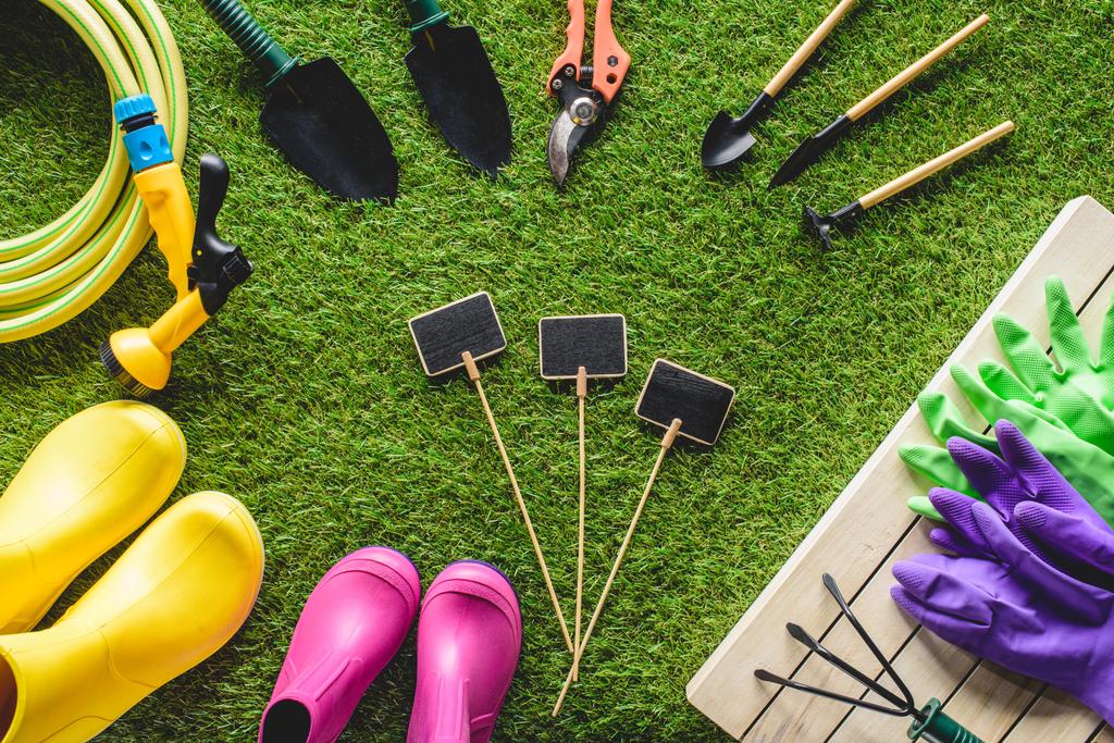 top view of empty blackboards surrounded by rubber boots, gardening equipment and protective gloves on grass - Photo, Image