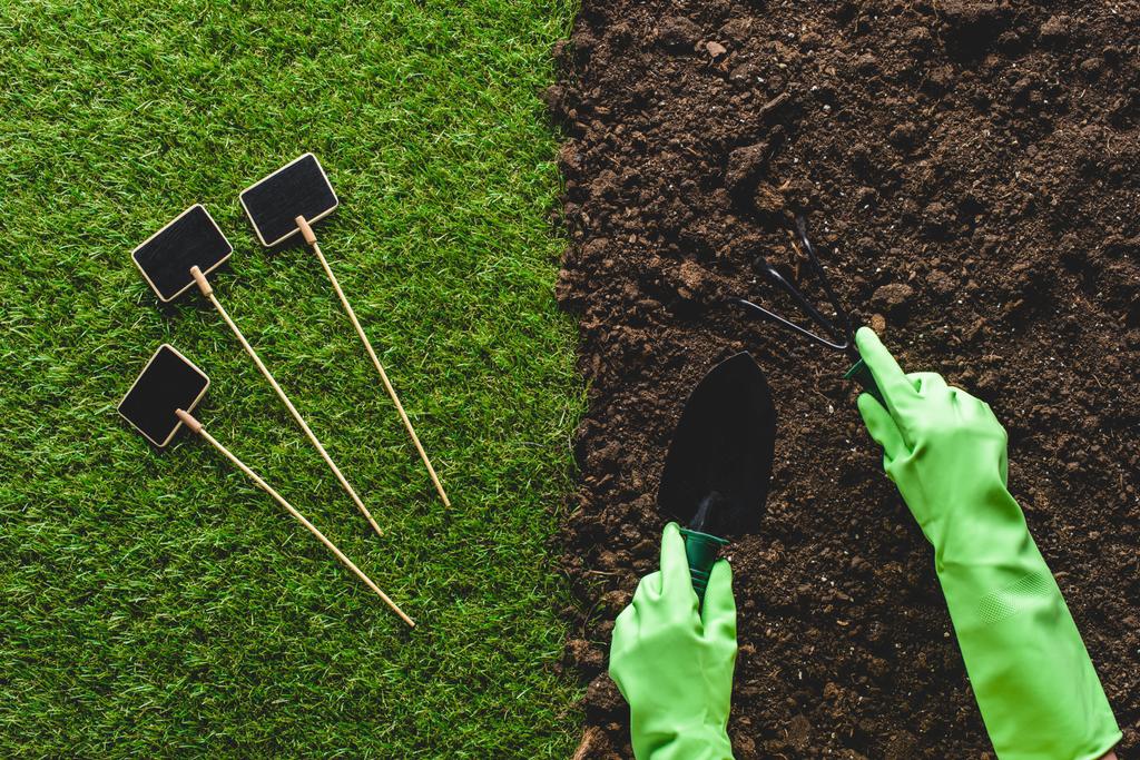 imagen recortada de jardinero en guantes de protección que trabajan con herramientas de jardinería y pizarras vacías en la hierba
 - Foto, imagen
