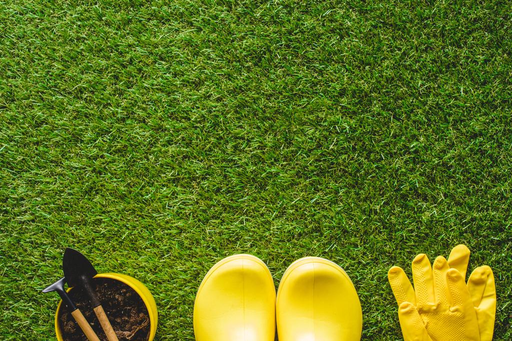 Ansicht von gelben Gummistiefeln, Schutzhandschuhen und Blumentopf mit Gartengeräten  - Foto, Bild