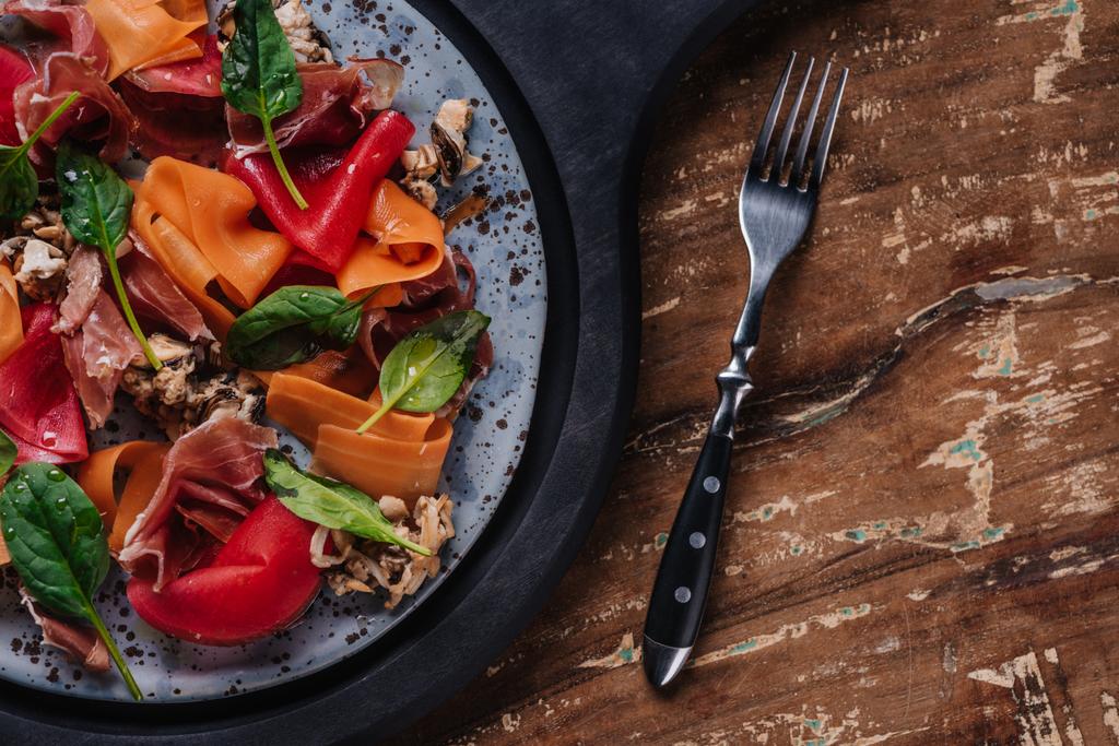 salada gourmet fresca com mexilhões, legumes e jamon na placa e garfo na mesa de madeira
  - Foto, Imagem