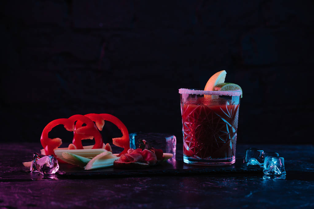 delicious bloody mary cocktail in glass and vegetables with melting ice cubes on dark surface  - Photo, Image