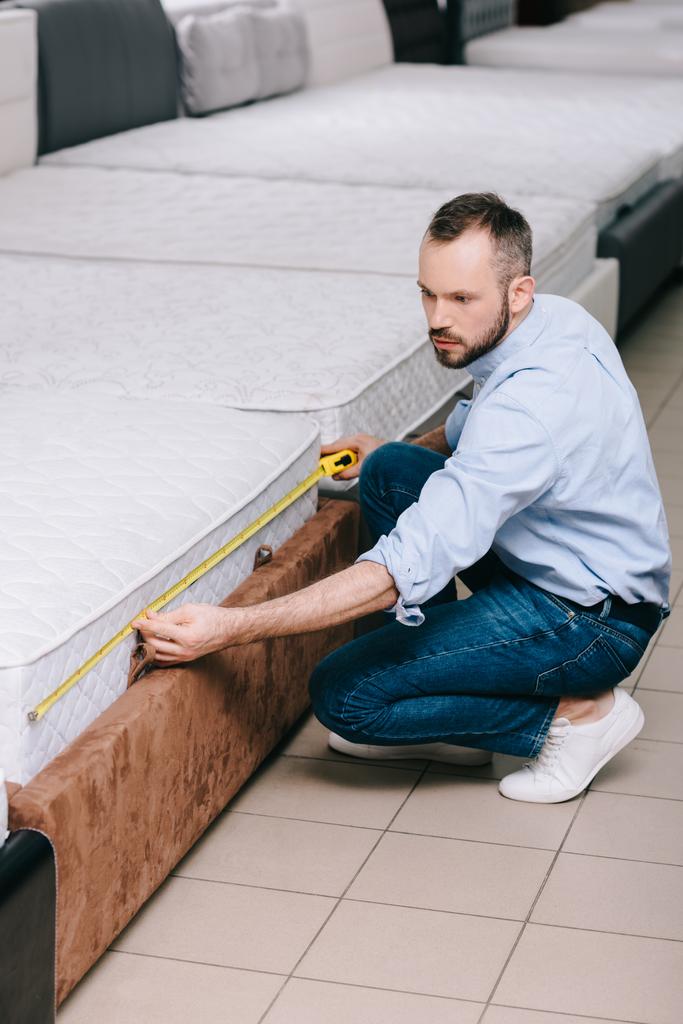 male shopper measuring orthopedic mattress with measure tape in furniture store - Photo, Image