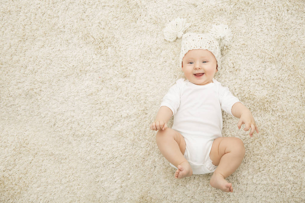 Bambino felice in cappello e pannolino sdraiato su sfondo tappeto, Ragazzo bambino sorridente in abbigliamento bianco, Bambino di sei mesi
 - Foto, immagini