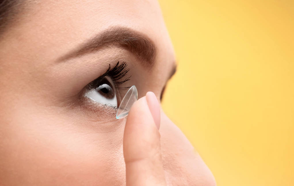 Mladá žena uvedení kontaktní čočky v oku na barvu pozadí, closeup - Fotografie, Obrázek