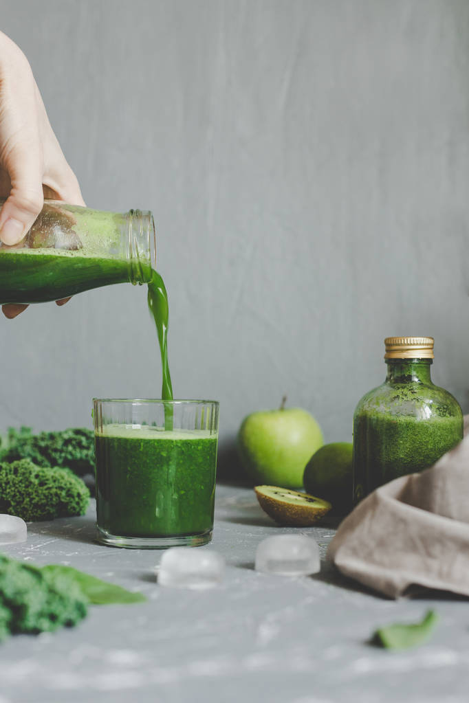 Mãos derramando smoothie verde saudável em um frasco. Conceito de alimentação limpa
 - Foto, Imagem