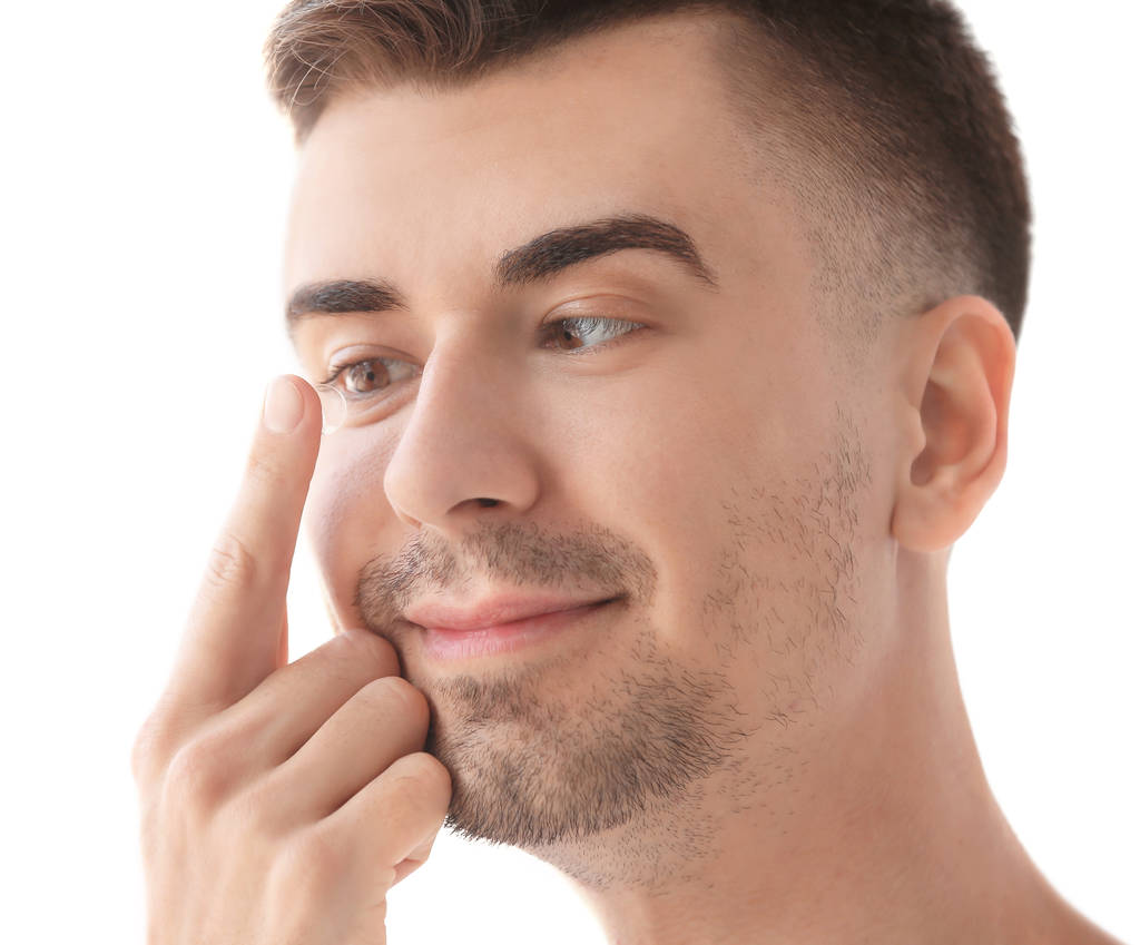 Mladý muž uvedení kontaktní čočky v oku na světlé pozadí - Fotografie, Obrázek