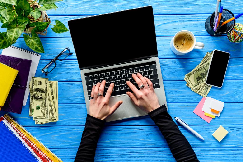 ręce, wpisując na klawiaturze laptopa na niebieski drewniany stół z papeterii i pieniądze - Zdjęcie, obraz