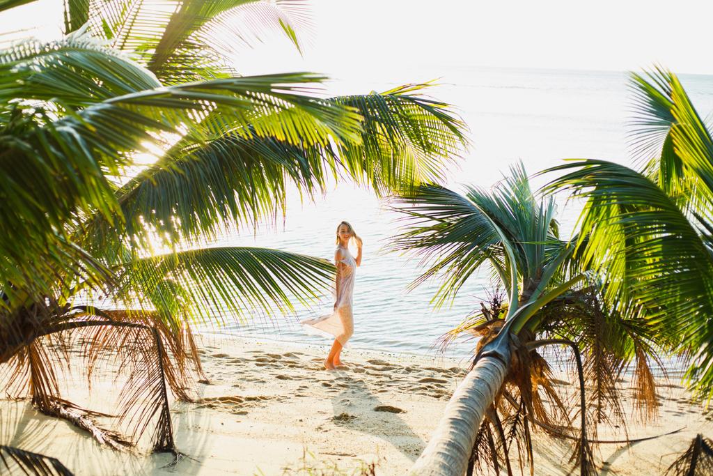 beautiful woman posing between palm trees on ocean beach - Photo, Image