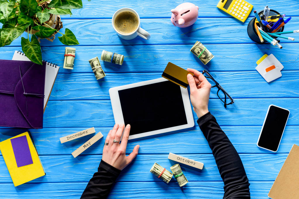 Hände mit Tablet und Kreditkarte auf blauem Holztisch mit Geld - Foto, Bild