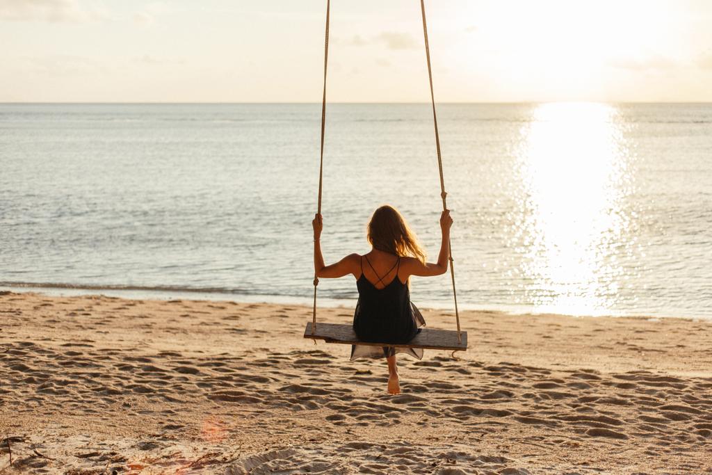 vue arrière de la femme sur le swing à la plage de l'océan pendant le coucher du soleil
 - Photo, image