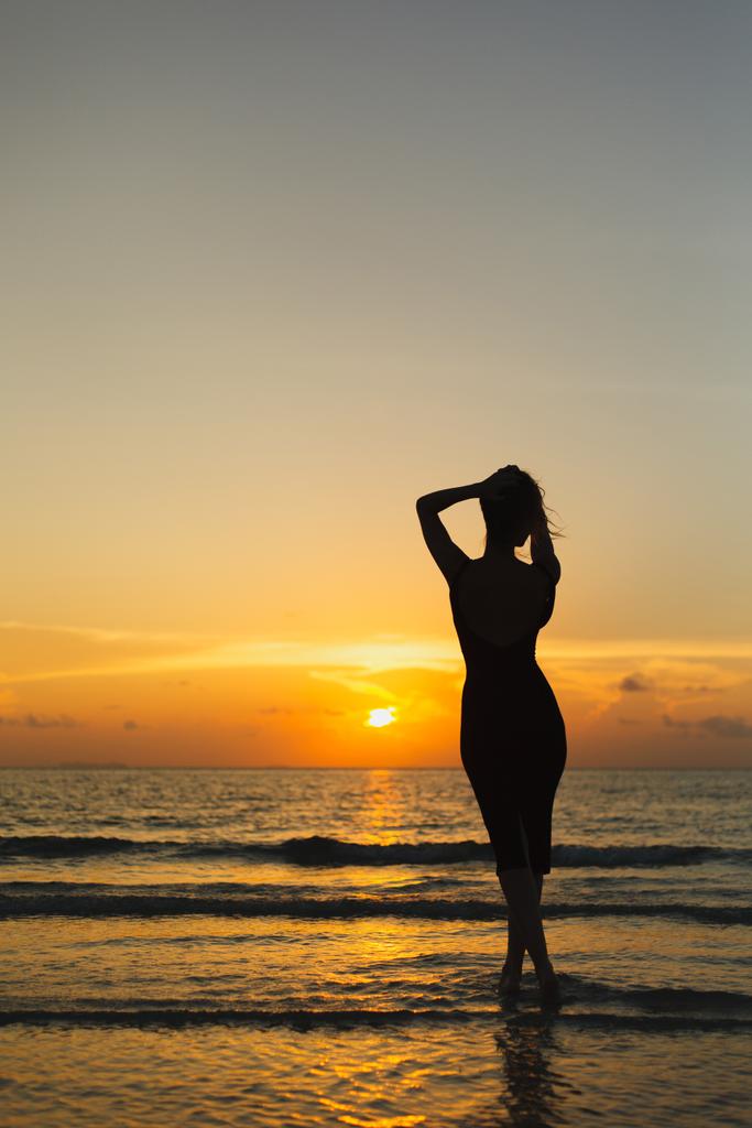 Rückansicht der Silhouette einer Frau, die bei Sonnenuntergang im Meer posiert - Foto, Bild