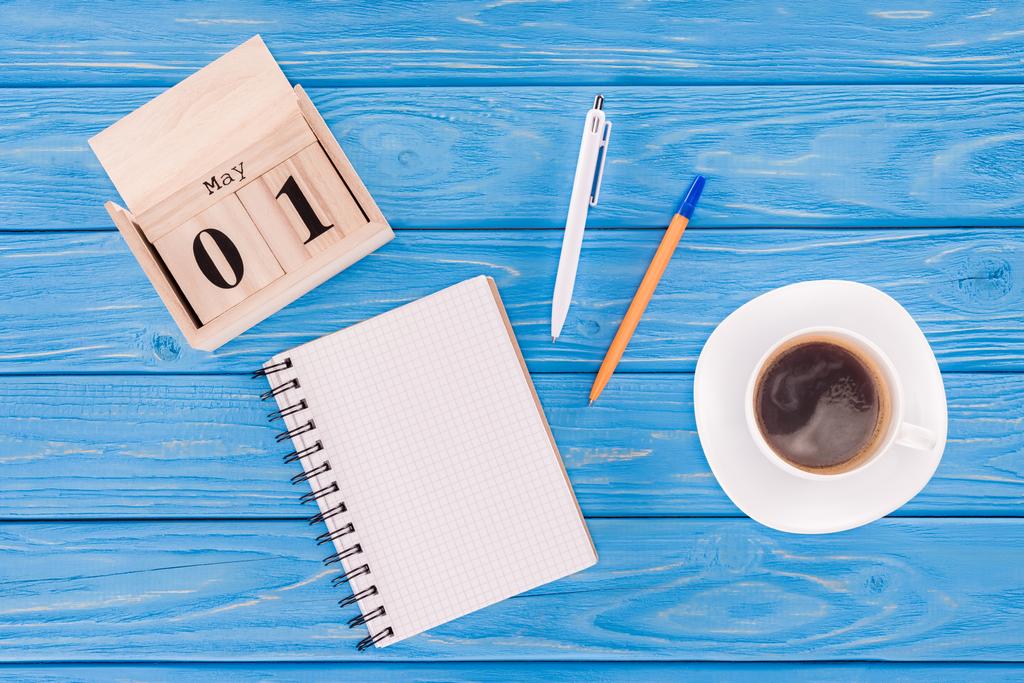 κάτοψη του ξύλινο ημερολόγιο με την ημερομηνία της 1ης Μαΐου, φλιτζάνι καφέ, κενό βιβλίο και στυλό, εργατική ημέρα έννοια  - Φωτογραφία, εικόνα