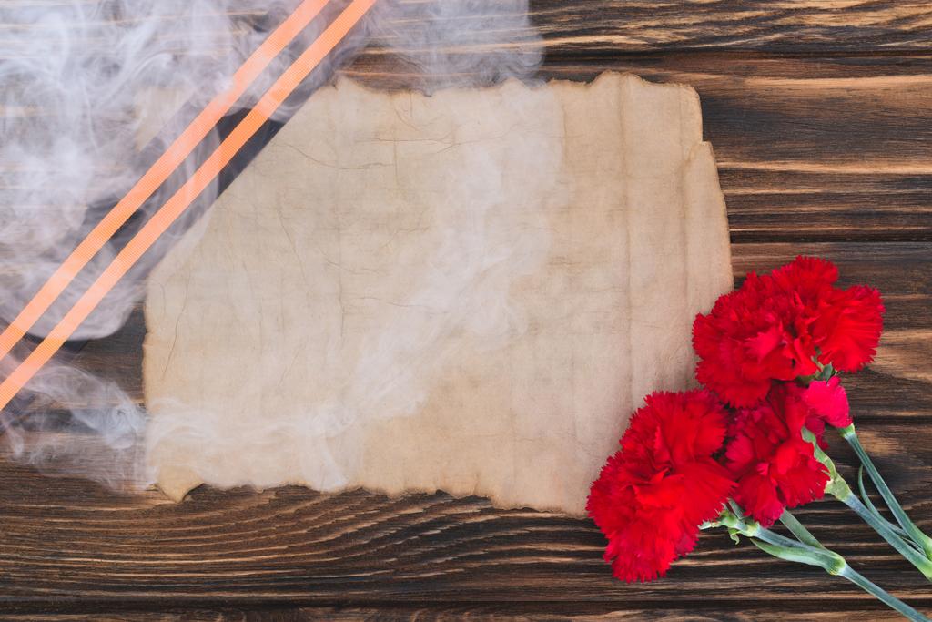 дым над Георгиевой лентой, старая пустая бумага и гвоздики на деревянной поверхности
 - Фото, изображение