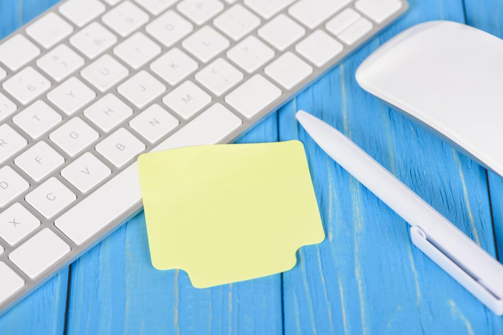 Nahaufnahme von leerem Notizpapier, Stift, Computertastatur und Maus auf blauer Holzoberfläche - Foto, Bild