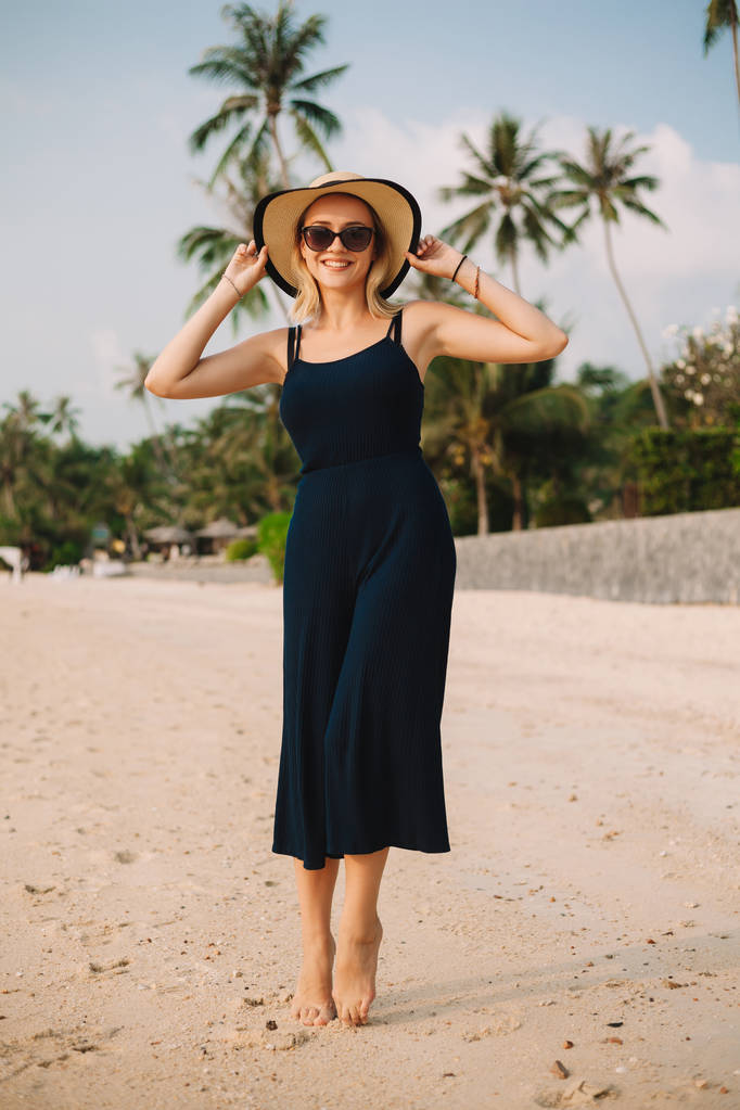 Happy krásná žena v šatech dotýká klobouk na písčité mořské pláži - Fotografie, Obrázek
