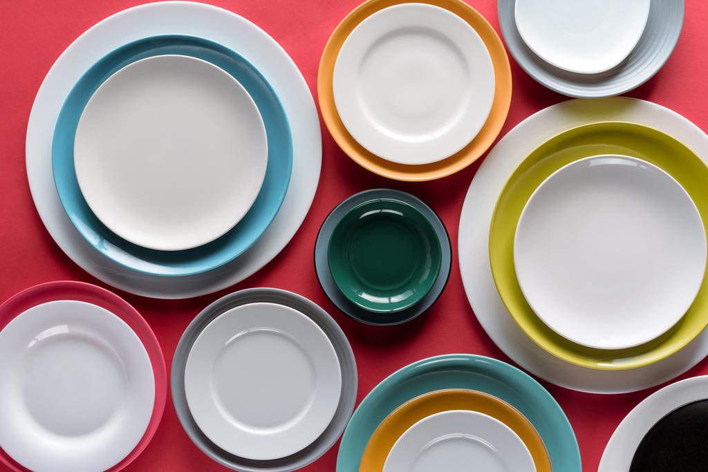 White and colorful plates of different sizes on red background - Photo, Image