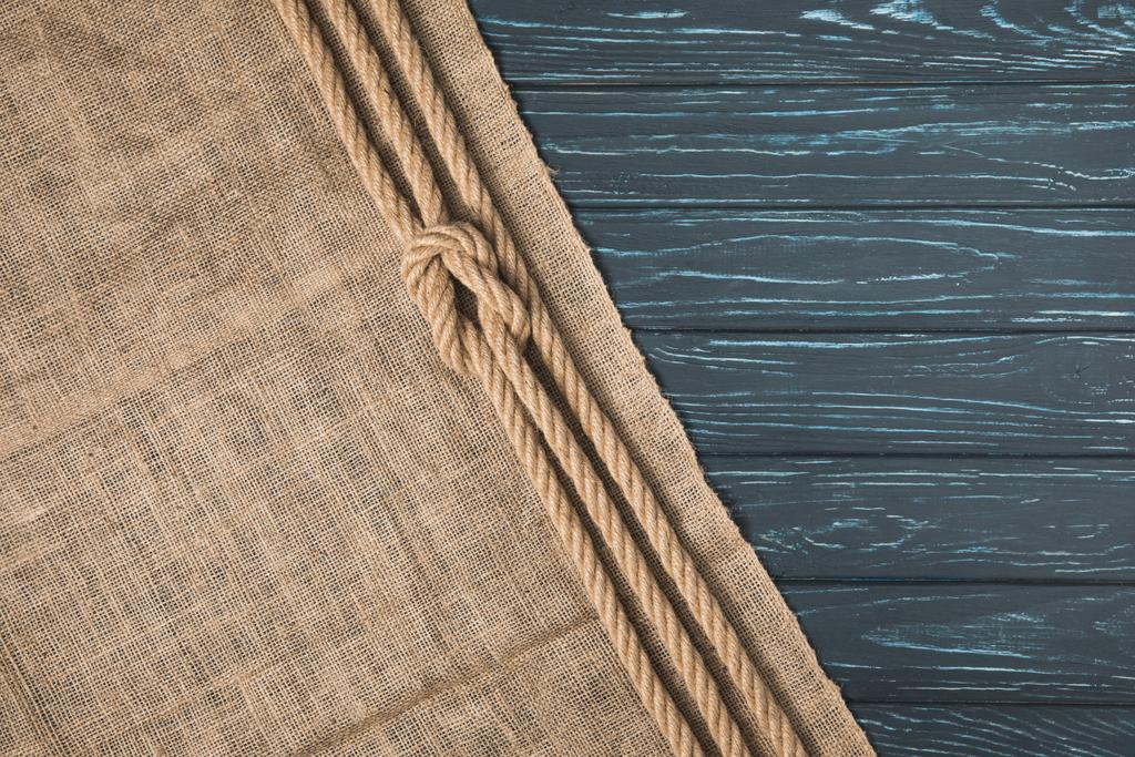 bovenaanzicht van geknoopte bruin nautische touw op zak op houten achtergrond - Foto, afbeelding