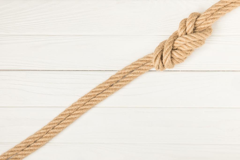 вид зверху на коричневу морську мотузку з вузлом на білій дерев'яній поверхні
 - Фото, зображення
