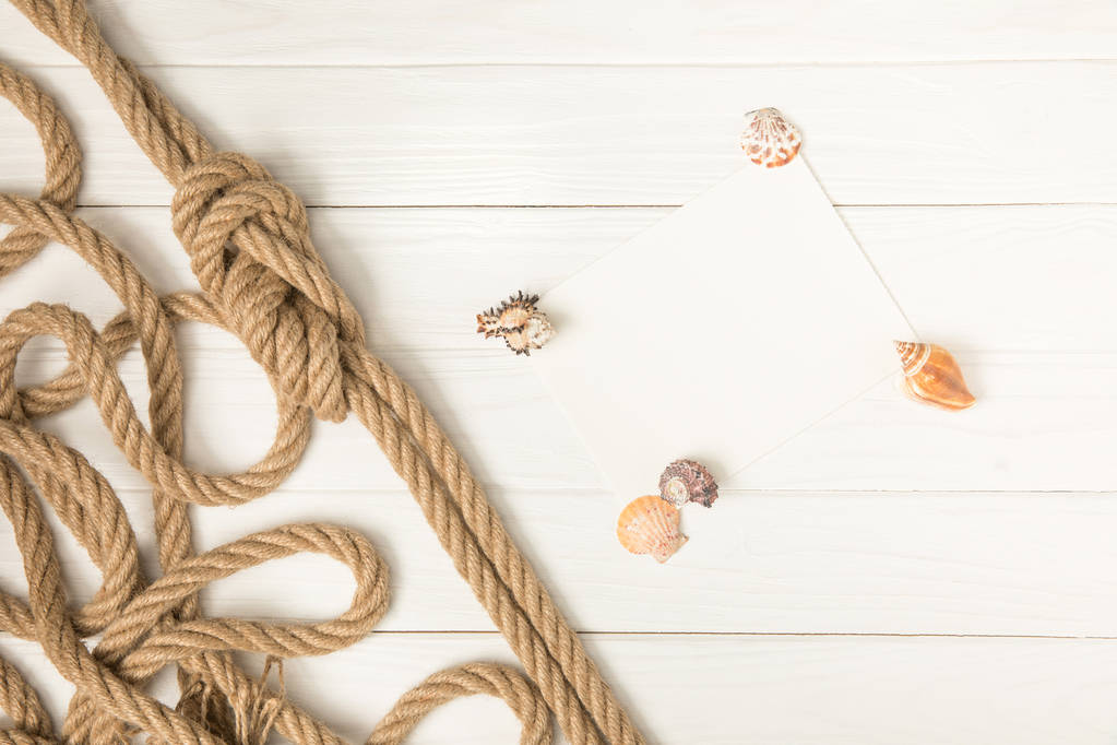 白い木製の表面に茶色の航海結び目ロープと貝殻で空の紙の上から見る - 写真・画像