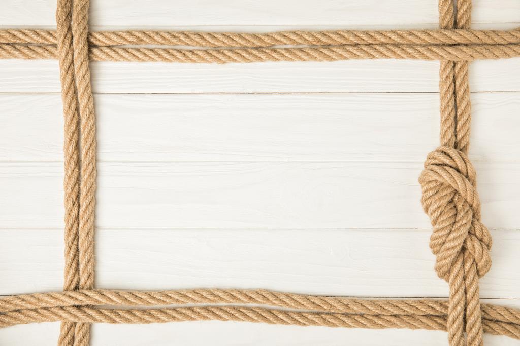 Ansicht des Rahmens von braunen nautischen Seilen mit Knoten auf weißem Holzhintergrund - Foto, Bild
