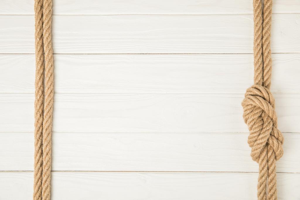 вид сверху на рамку из коричневых морских канатов с узлом на белом деревянном фоне
 - Фото, изображение