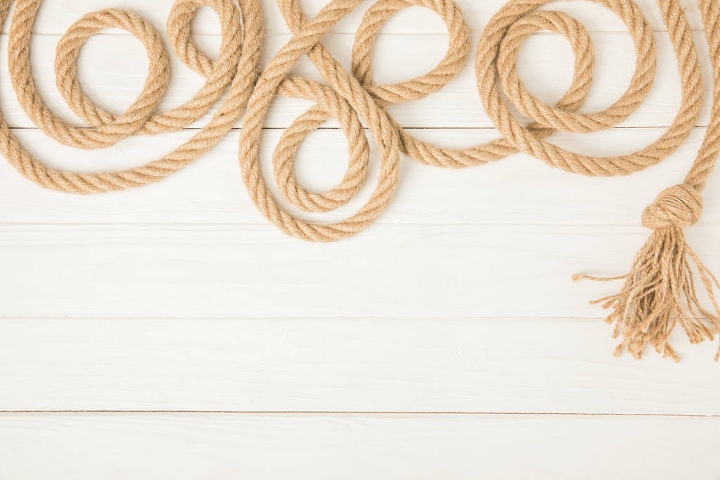 Draufsicht auf braunes nautisches geknüpftes Seil auf weißem Holzhintergrund - Foto, Bild