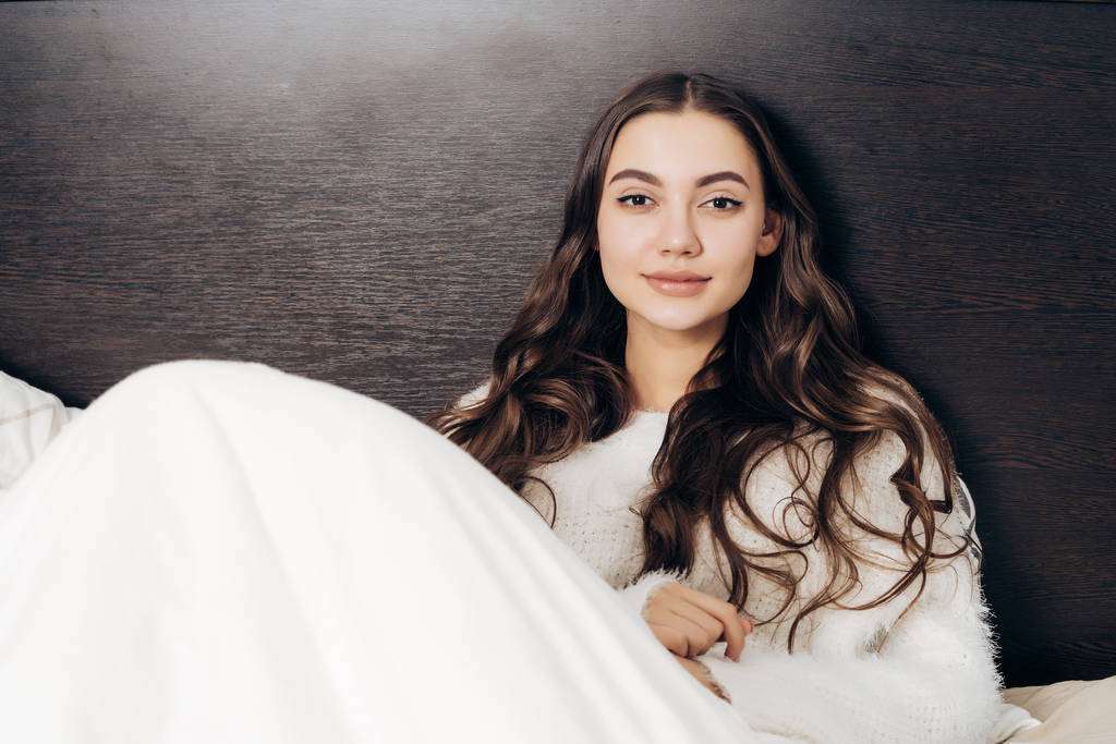 kaunis pitkätukkainen tyttö istuu sängyssä, lepää töiden jälkeen, hymyilee
 - Valokuva, kuva