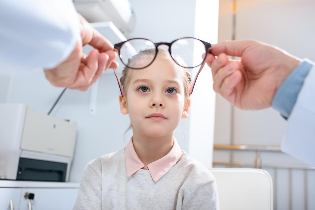 imagen recortada del oftalmólogo que usa gafas nuevas en el niño preadolescente en la clínica
 - Foto, Imagen