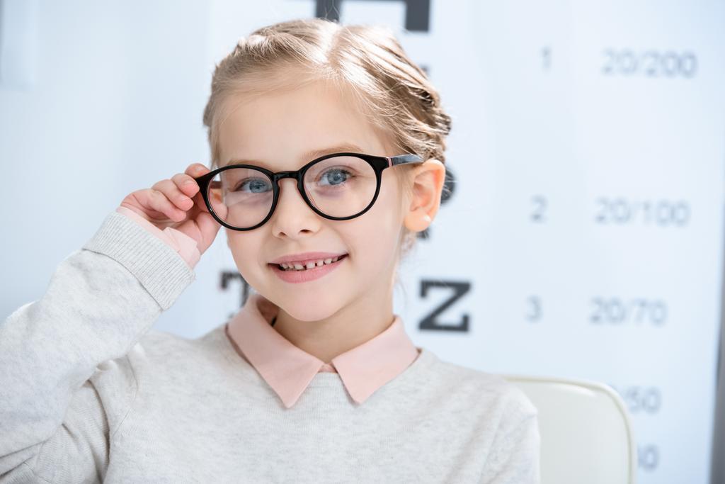 adorable enfant souriant regardant la caméra dans les lunettes à la salle de consultation oculiste
 - Photo, image