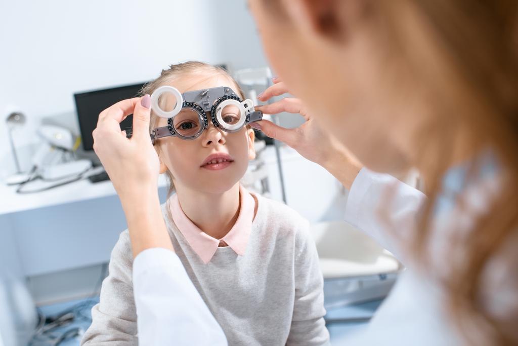 Selektiver Fokus des Augenarztes, der Kinderaugen mit Versuchsrahmen in der Klinik untersucht - Foto, Bild