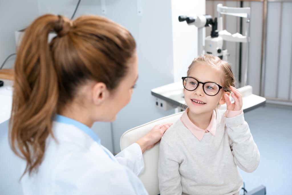Οφθαλμίατρος και χαμογελαστό παιδί σε γυαλιά στην οπτική  - Φωτογραφία, εικόνα