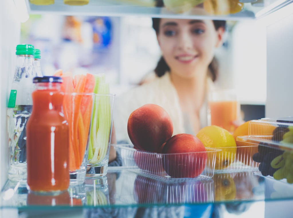 Портрет жінки, що стоїть біля відкритого холодильника, повний здорової їжі, овочів та фруктів. Портрет жінки
 - Фото, зображення