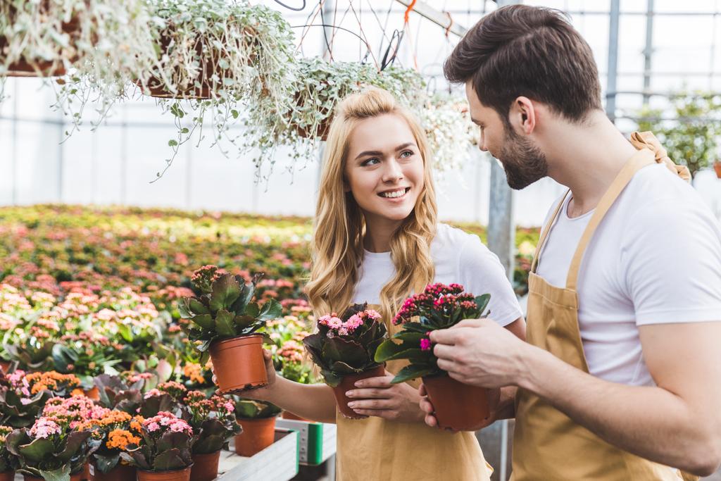 Jardineiros sorridentes que mantêm potes com flores em estufa
 - Foto, Imagem