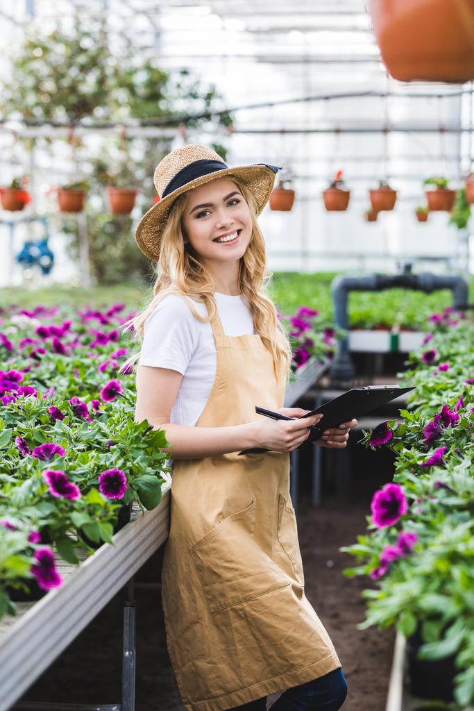 Blonde woman with clipboard filling order of flowers in greenhouse - Photo, Image