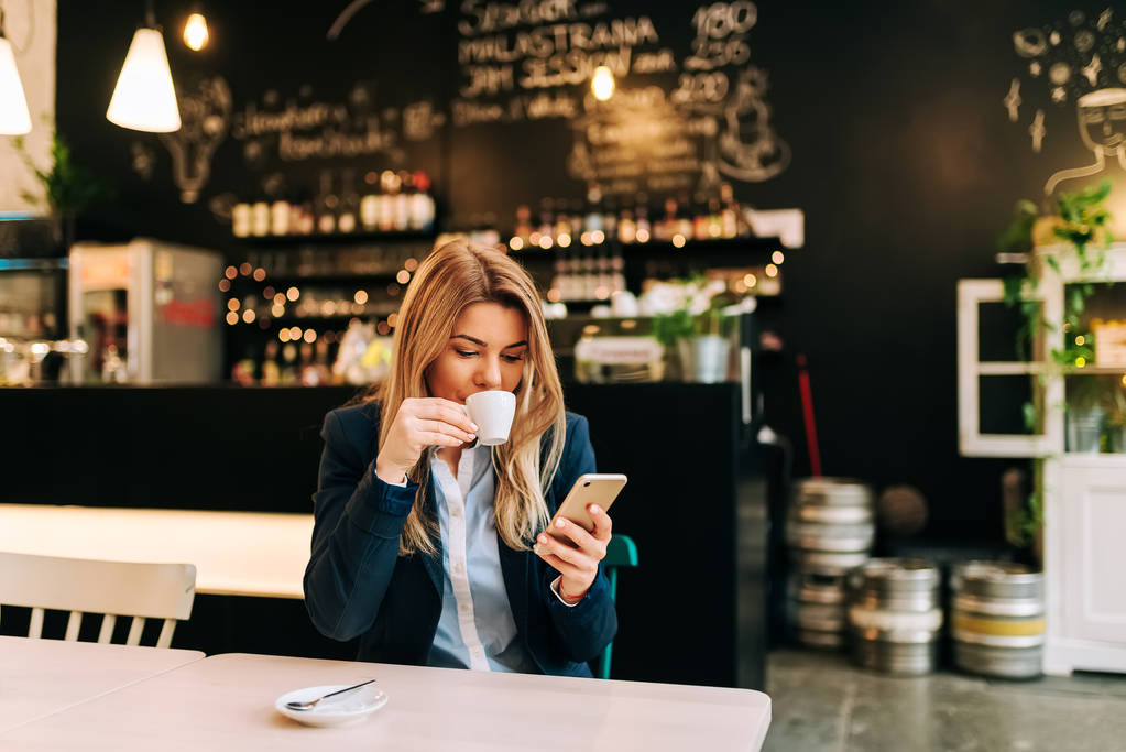 Empresaria bebiendo café y usando smartphone en restaurante
 - Foto, imagen
