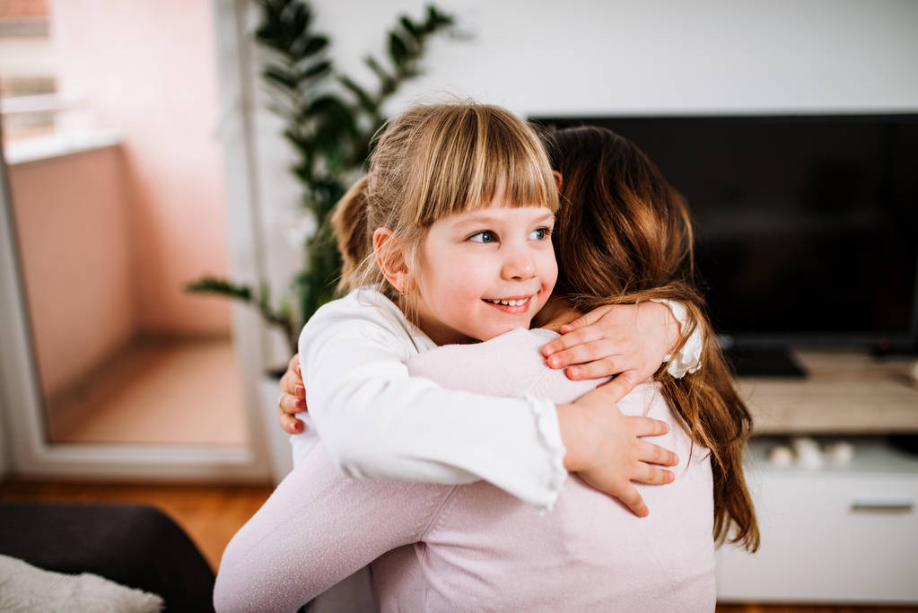 Tochter umarmt Mutter im Wohnzimmer zu Hause - Foto, Bild